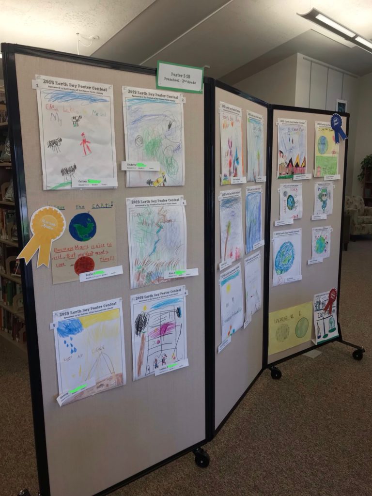 Earth Day poster entries displayed on a movable wall in the library